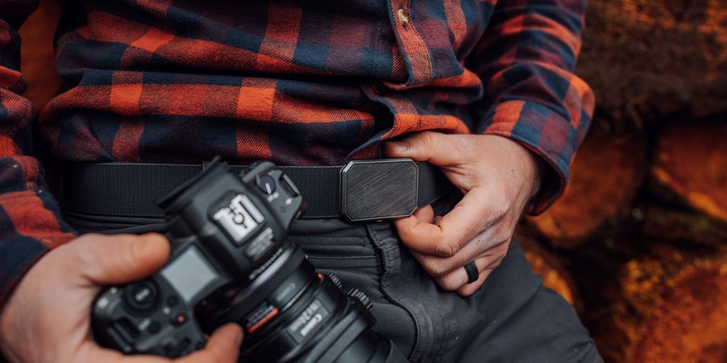 Person holding a camera, adjusting a belt on clothing.