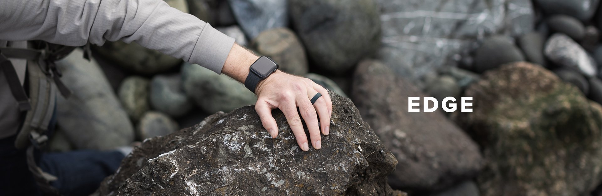 A man wearing an edge ring and black watch band climbs up some rocks
