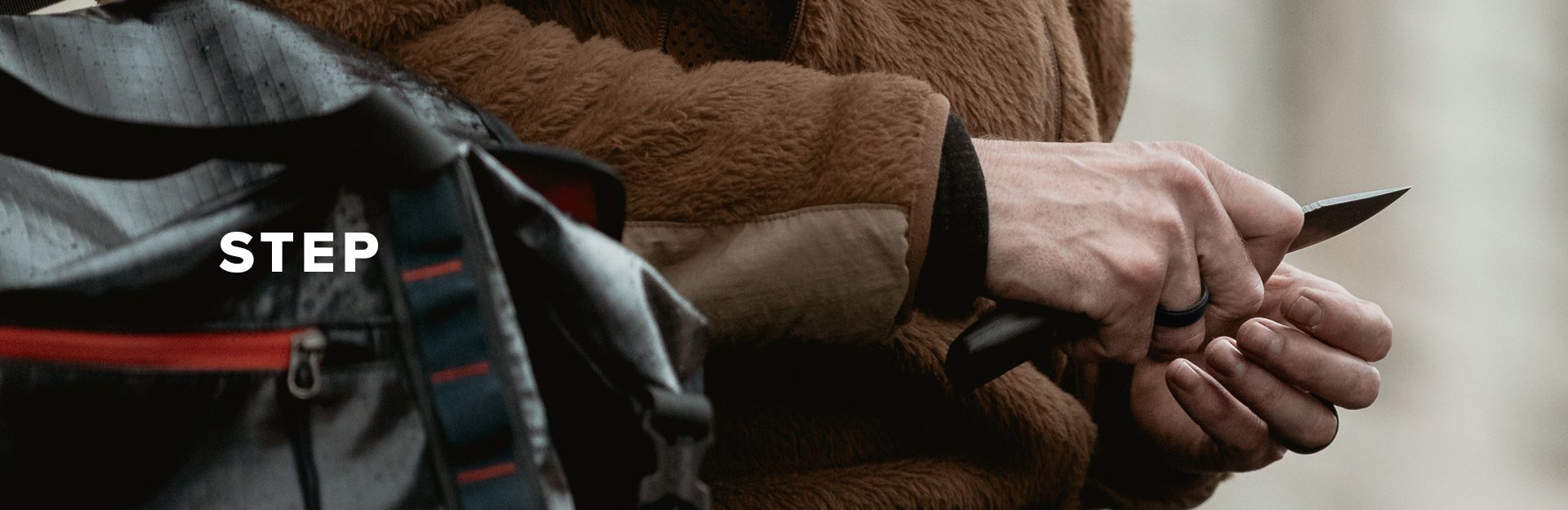 Step, a man sharpens his hunting knife with his backpack in the foreground