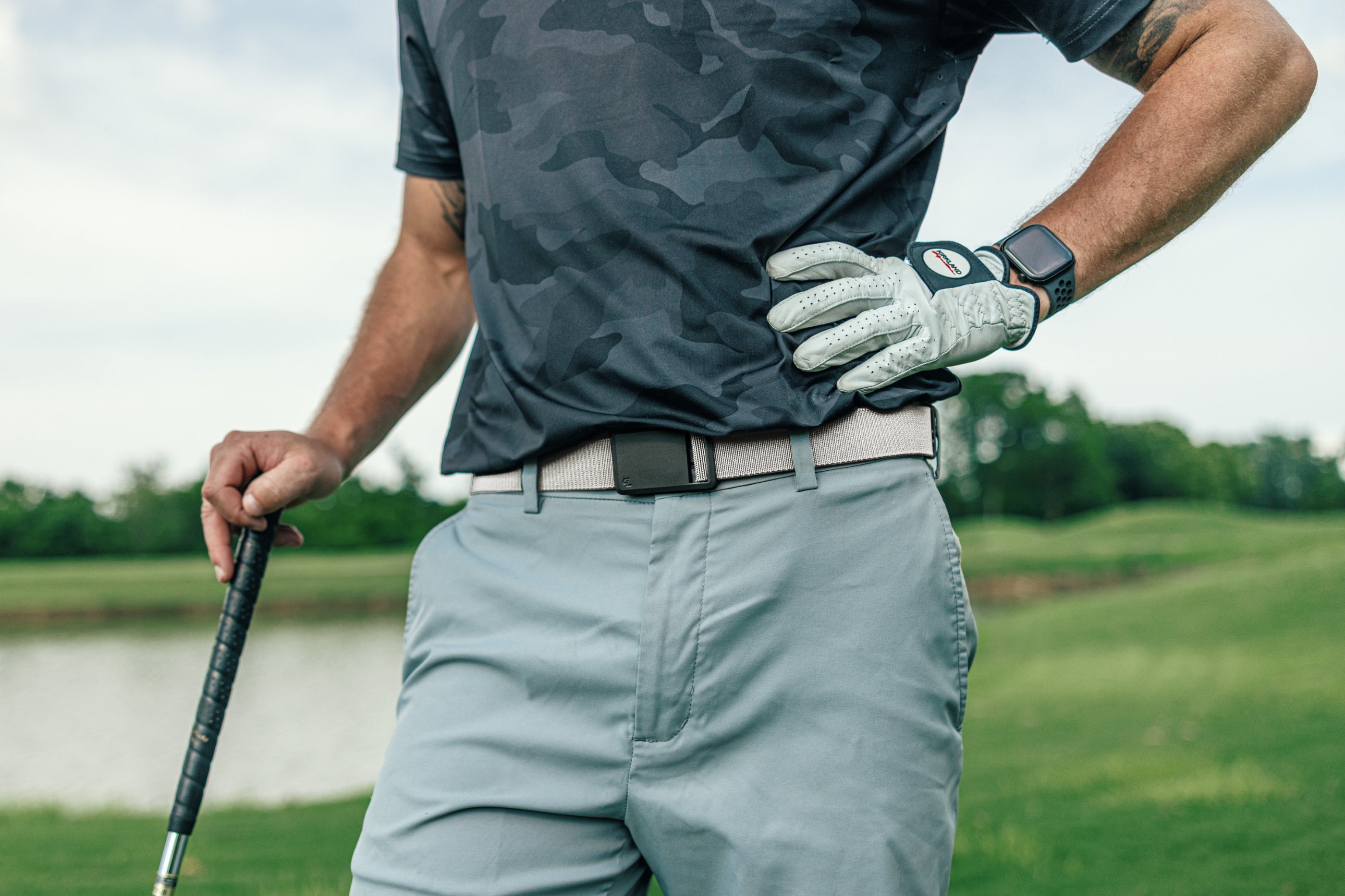 Person on a golf course wearing a dark camo shirt, light gray pants, and a white glove.