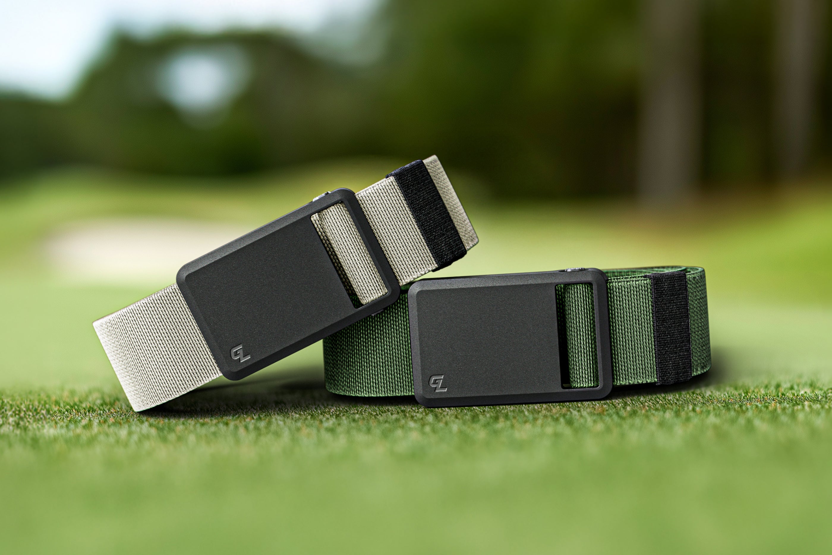 Two belts, one gray and one green, on a grassy background.