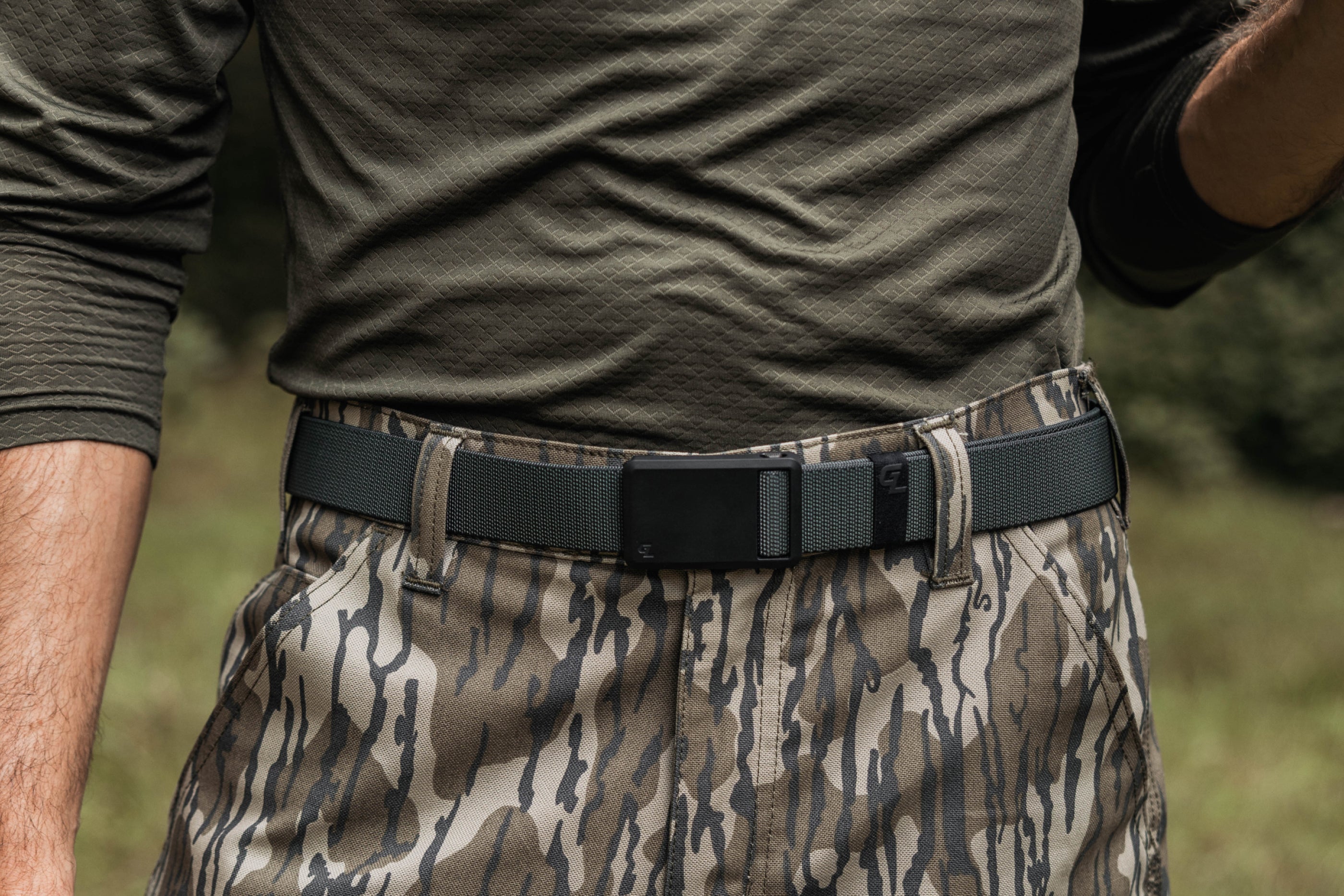 Person wearing camouflage pants and a green shirt with a Groove Belt Ultra in Coal Dust