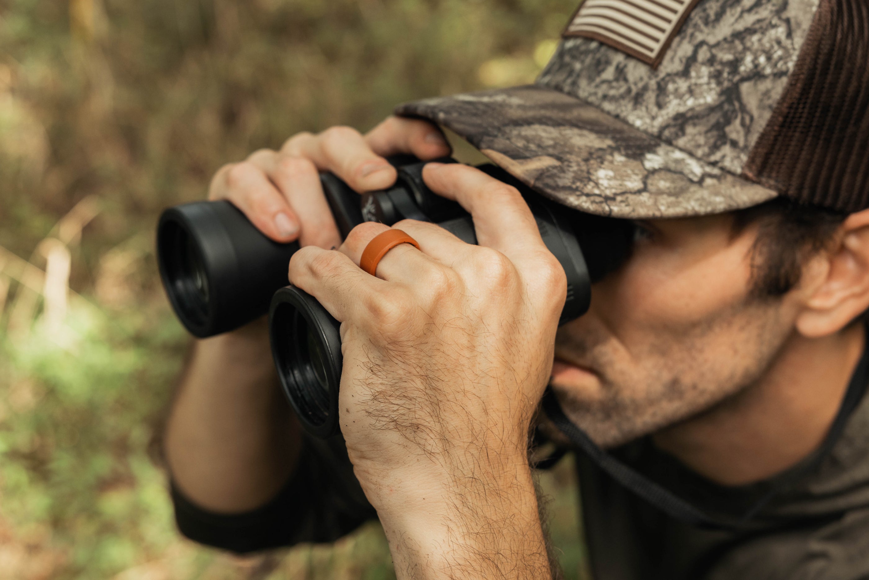 Person in camouflage hat using binoculars in a forest setting