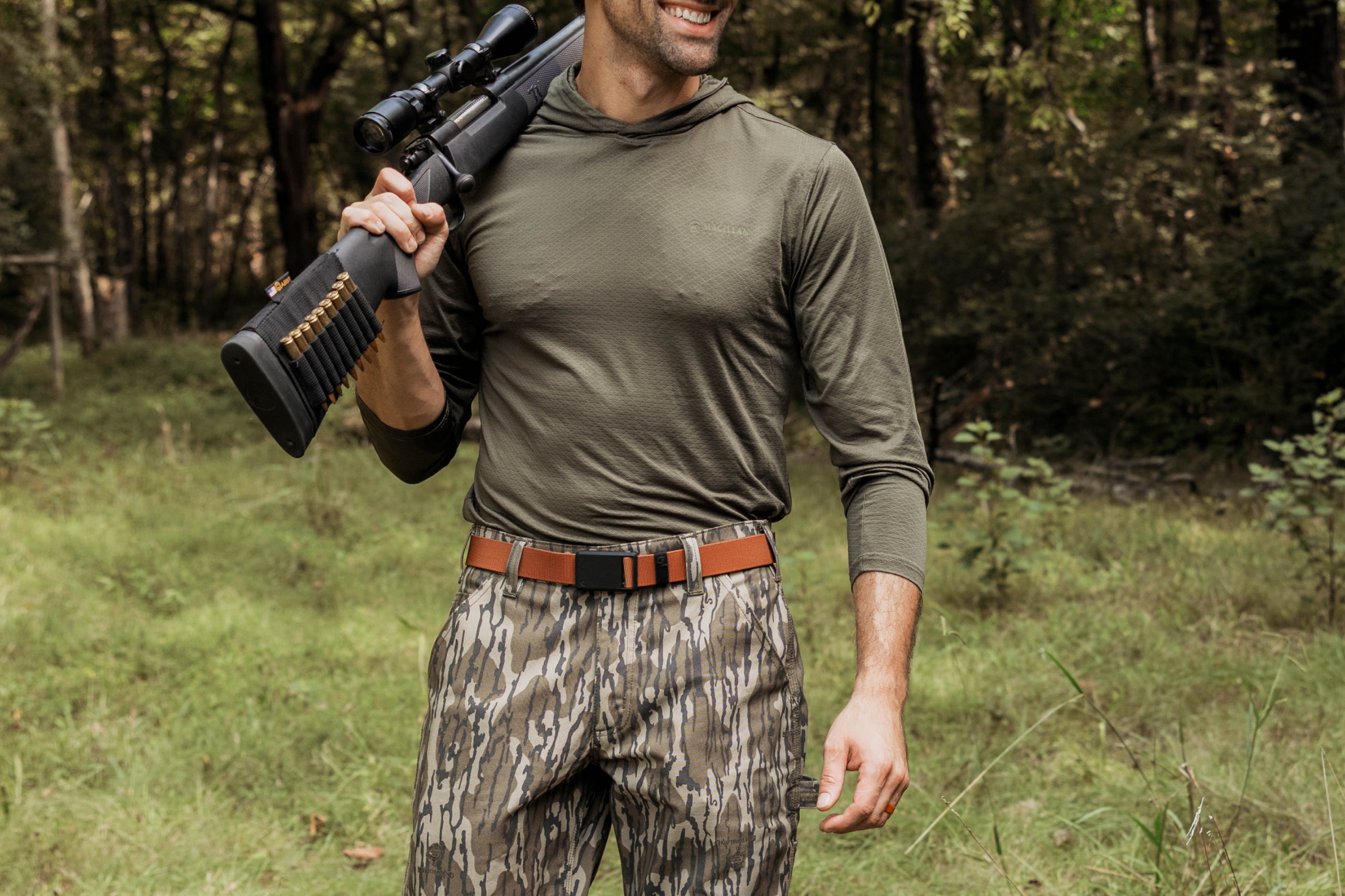 Man in hunting gear holding a rifle in a forest setting