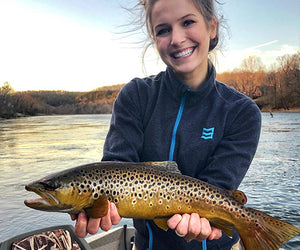 Cara Harper poses with a trout fished from the river behind her
