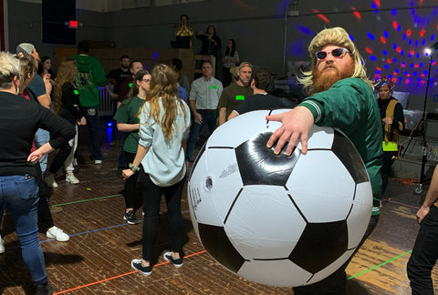 Groove guy in a yellow wig holding a giant soccer ball at a mandatory fun
