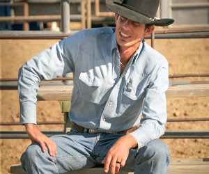 JB Mauney sits on a fence at an arena, with a hand on his knee