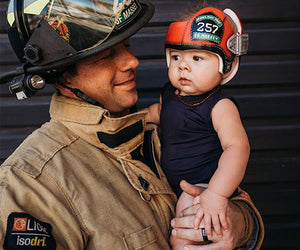 Jordan Massey, in firefighter gear, holds his young child up and looks at him