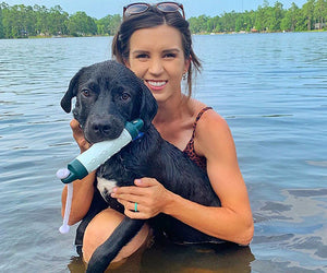 Ashley Hall holds her black lab in a lake, while the dog holds a water toy in his mouth