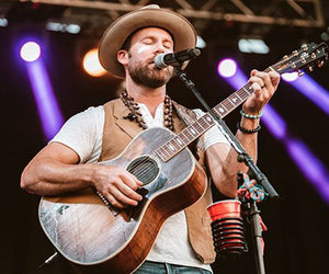 Drake White sings into a microphone with his eyes closed as he plays the guitar